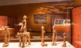 Five small medieval artifacts lined up in an exhibition case with an orange backdrop 